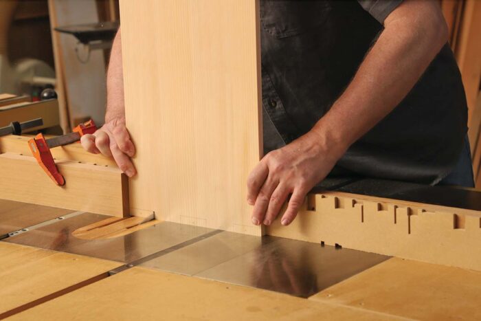 A piece of wood held on end being notched at the table saw.