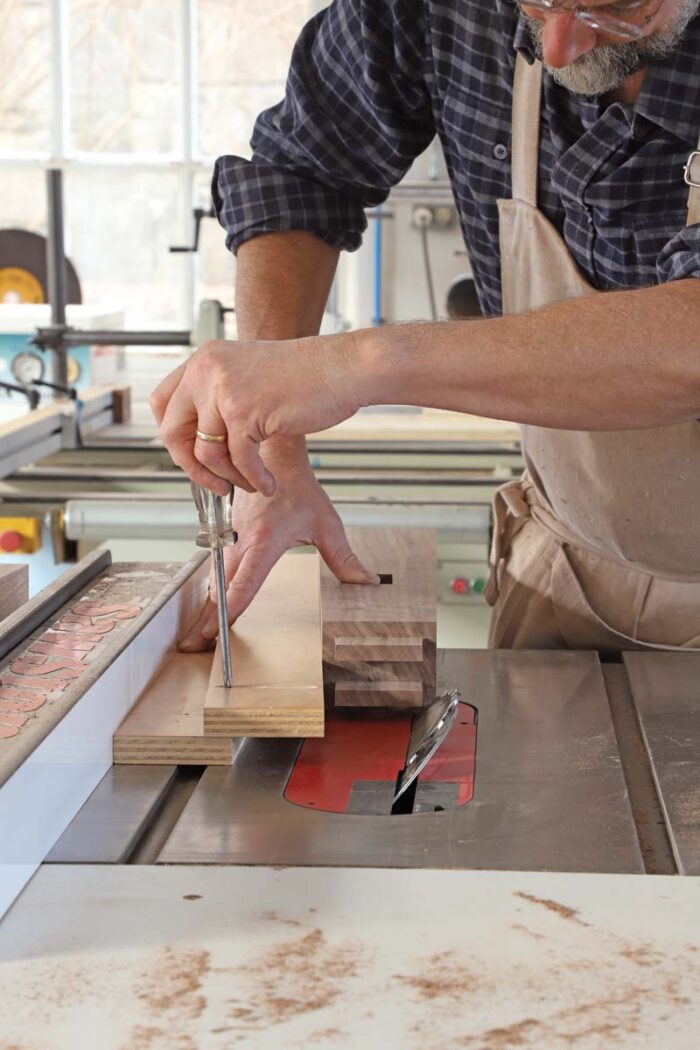 Tom sets up the angle on a shop made tapering jig for the table saw. He tightens a screw with a screwdriver, locking in the angle. 