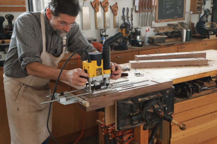 Tom uses a cove bit in a plunge router, as well as an edge guide, to rout cove cuts on either side of the trestle foot. 