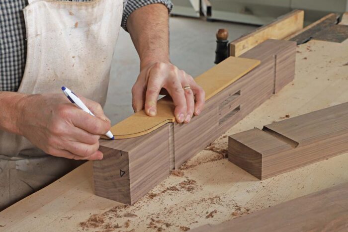 Tom uses a shop made pattern to trace the profile for the top of the foot onto one end of the foot. The cove that was previoulsy cut on the foot aligns where the pattern should go. 