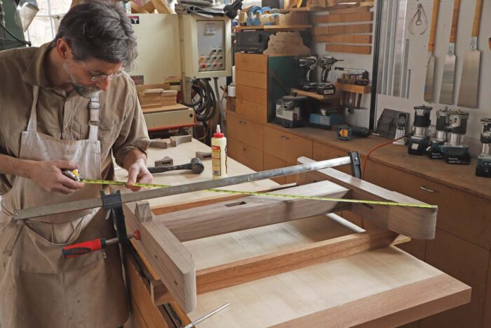 Tom clamps up the trestle leg while it sits on two winding sticks, using a measuring tape to check for square.