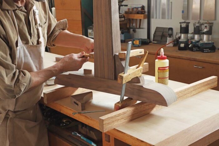 Tom clamps one corbel in place, between the foot and the leg. One clamp is placing downward pressure and the other pressure to the leg.