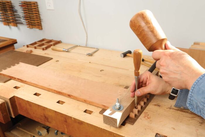 A board is clamped the bench and the dovetails are being chopped out.