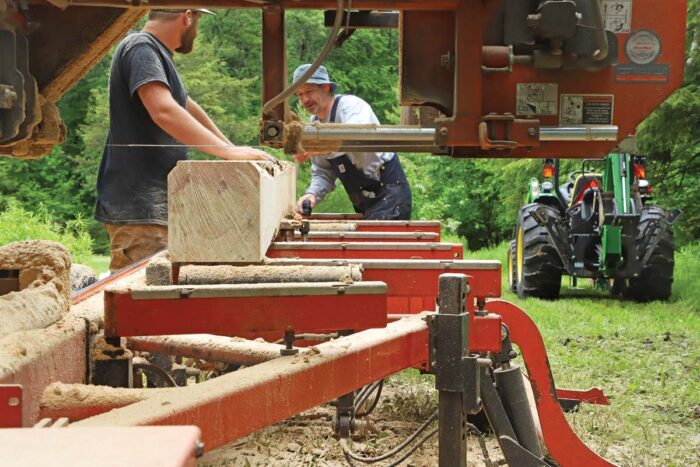 Two men milling a log on an orange saw mill. 