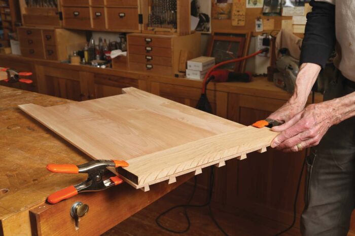 Chris uses spring clamps to attach a clamping caul to the top of the sides, where dovetails have been cut. 