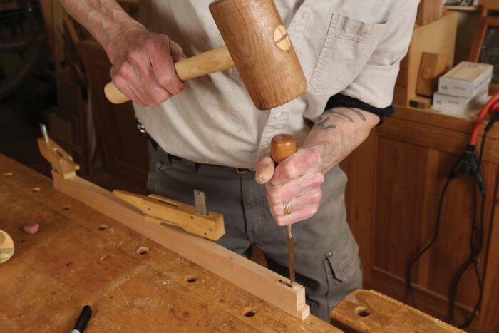 Chris uses a mallet to chisel a mortise in the parts that will make a web frame. 