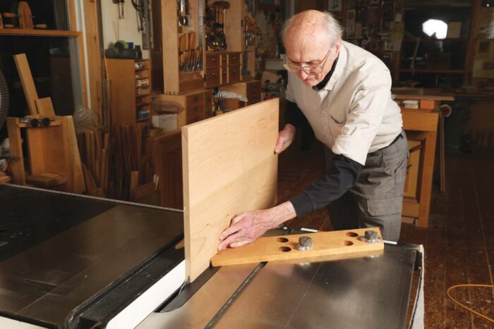 Chris uses a shop made featherboard to help him cut one shoulder of a rabbet on the tablesaw. he is holding the piece vertically. 