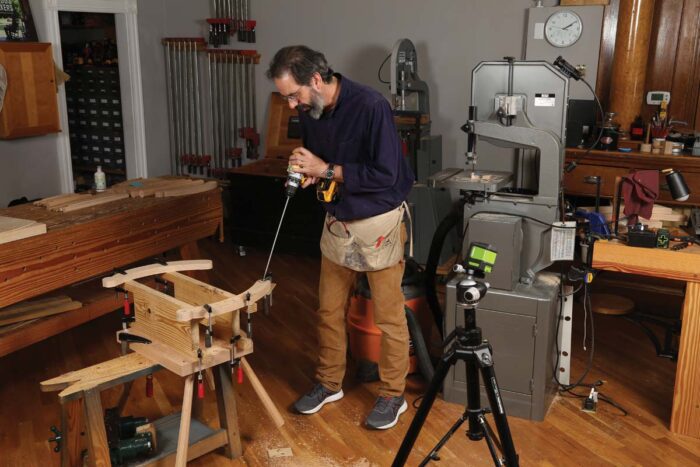 Chris is using a very (VERY!) long drill bit to drill in the arms. He seems to have recovered from his previous hunching over.