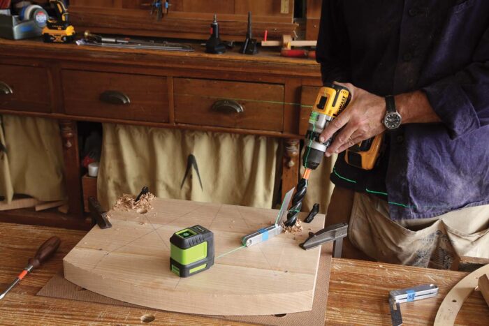 A drill is being used to create a mortise in the seat blank. A laser and a bevel gauge are used to guide the drilling action. Pew pew!