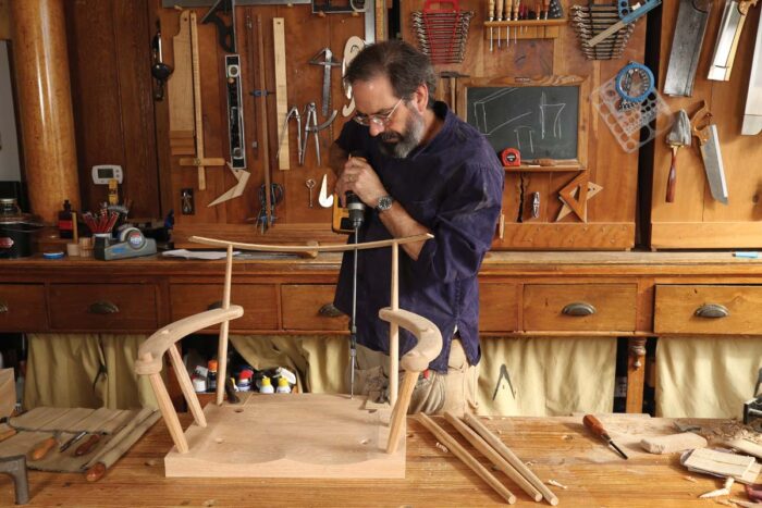 The unbelievably long drill bit is back and holes are being drilled with the bit passing through the top template into the chair seat.