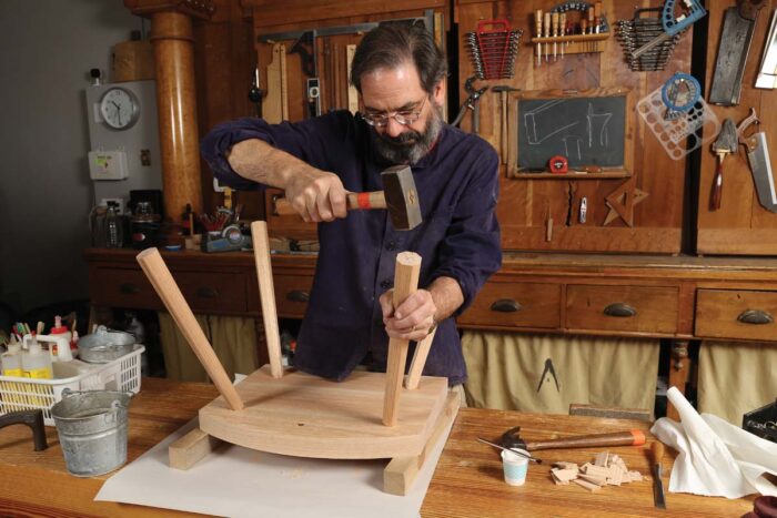 The chair legs are being hammered into place with a mallet.