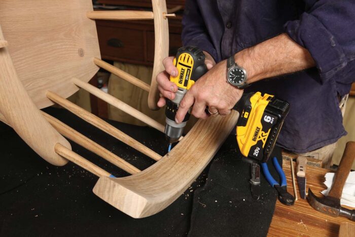 A reasonably sized drill bit is being used to drill a small hole in the chair back where the center stick is attached. 