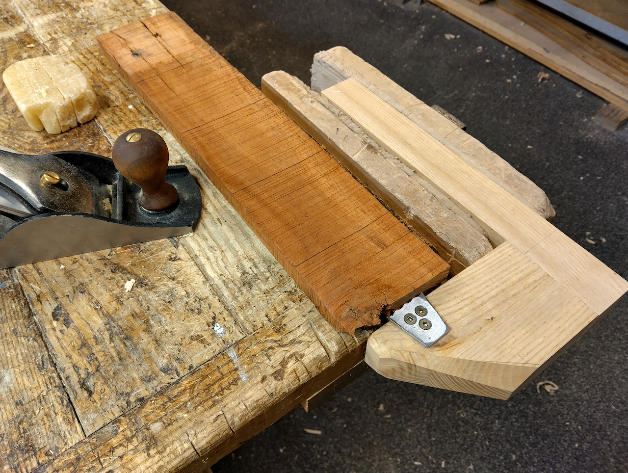 A jack plane sits next to a rough board.