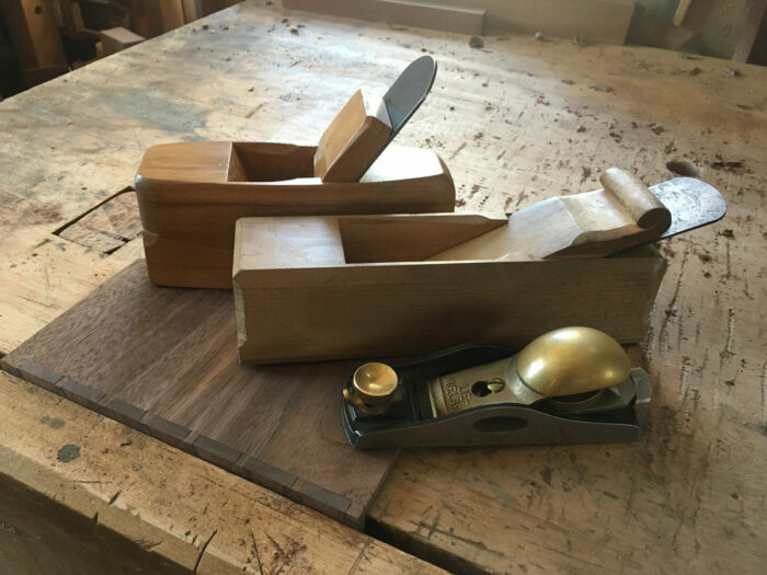 a photo of three planes lined up. Two wooden and one modern metal plane 